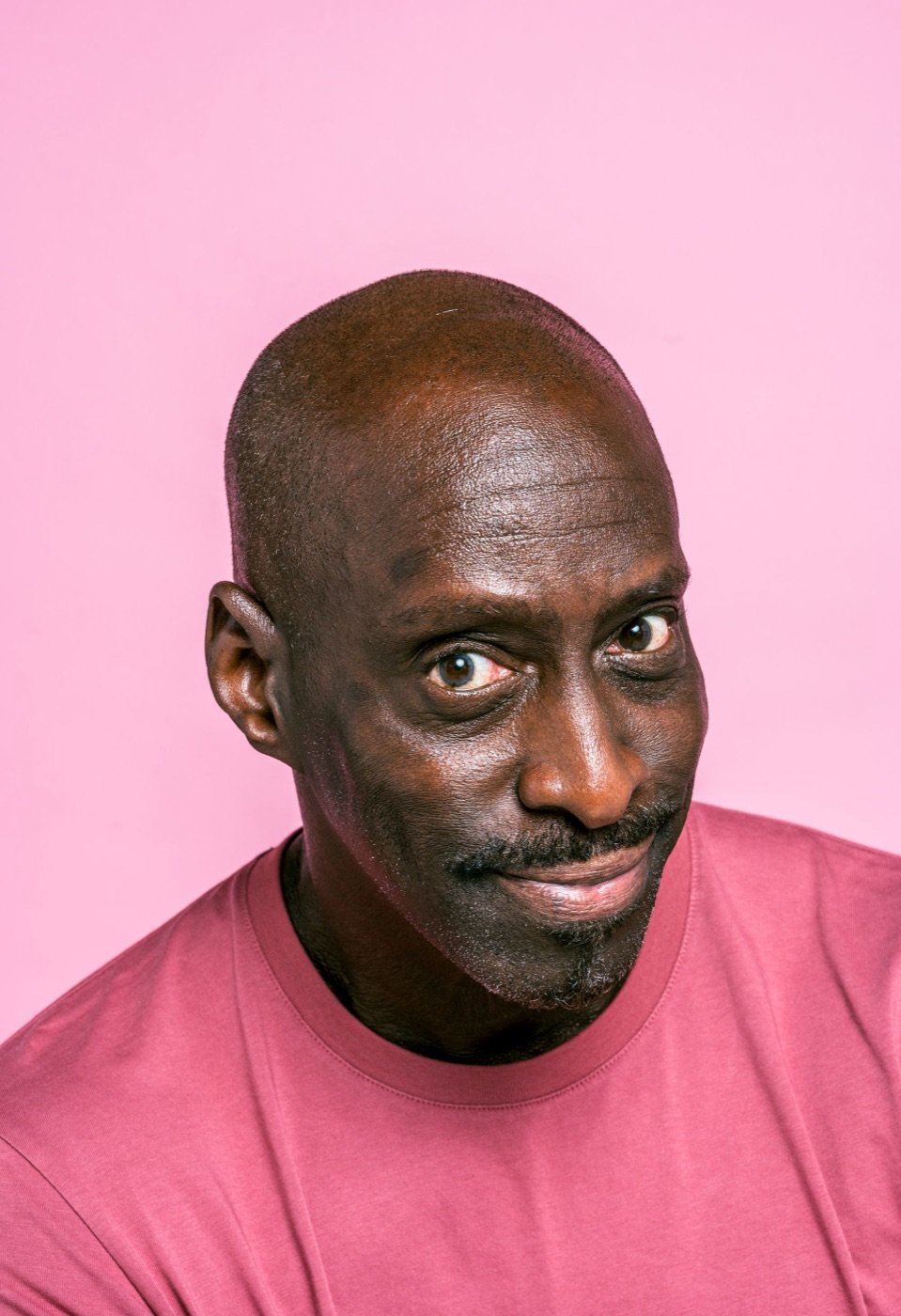 A man in a pink shirt on pink, eyes straight out