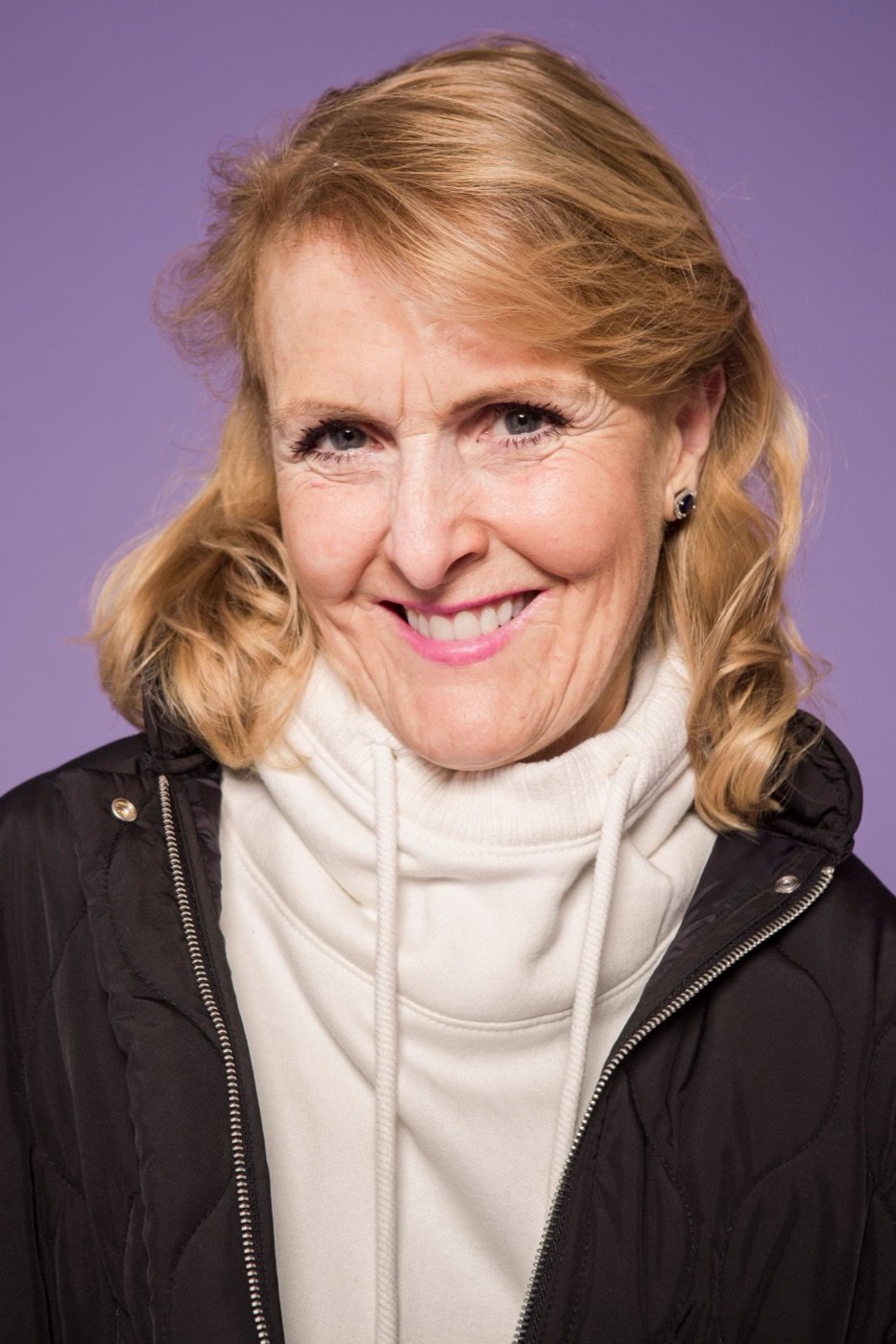 A woman with blonde hair, smiling, on purple