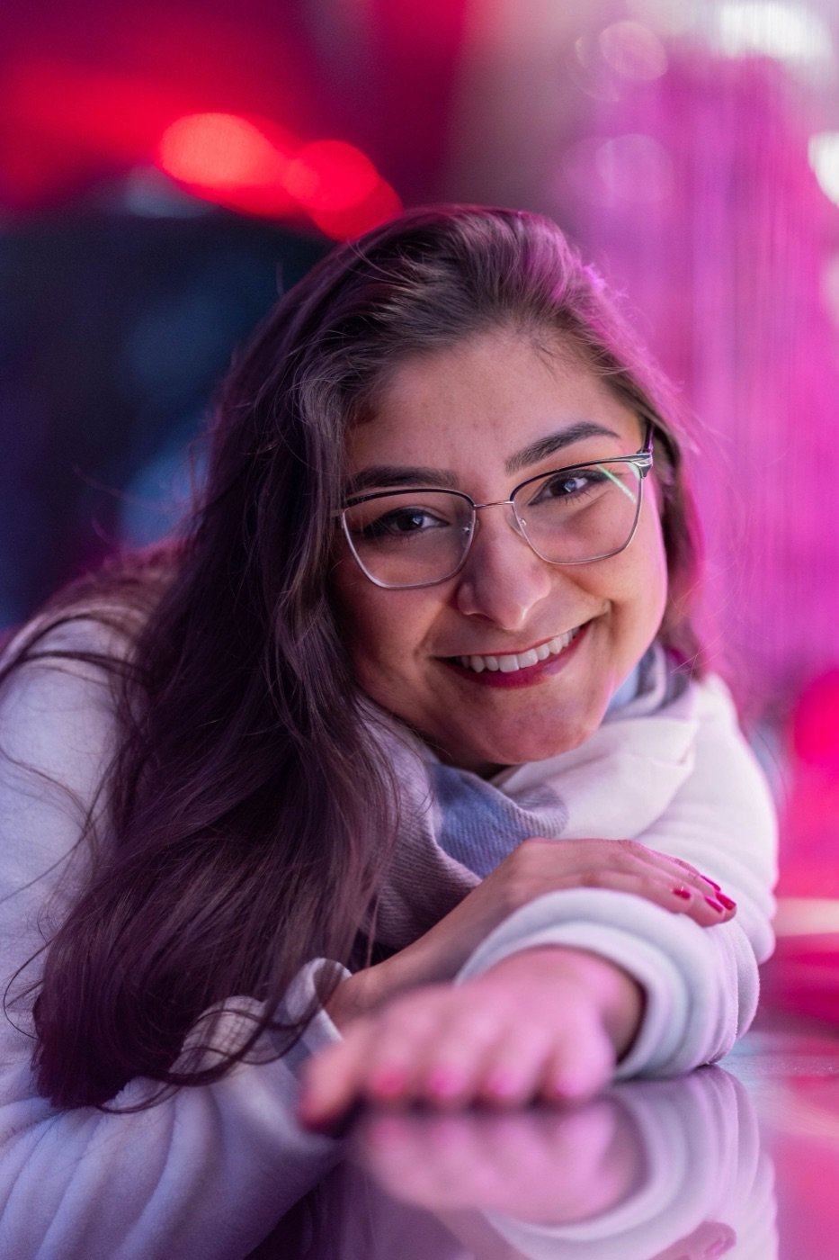 A woman in glasses, laughing, in pink neon