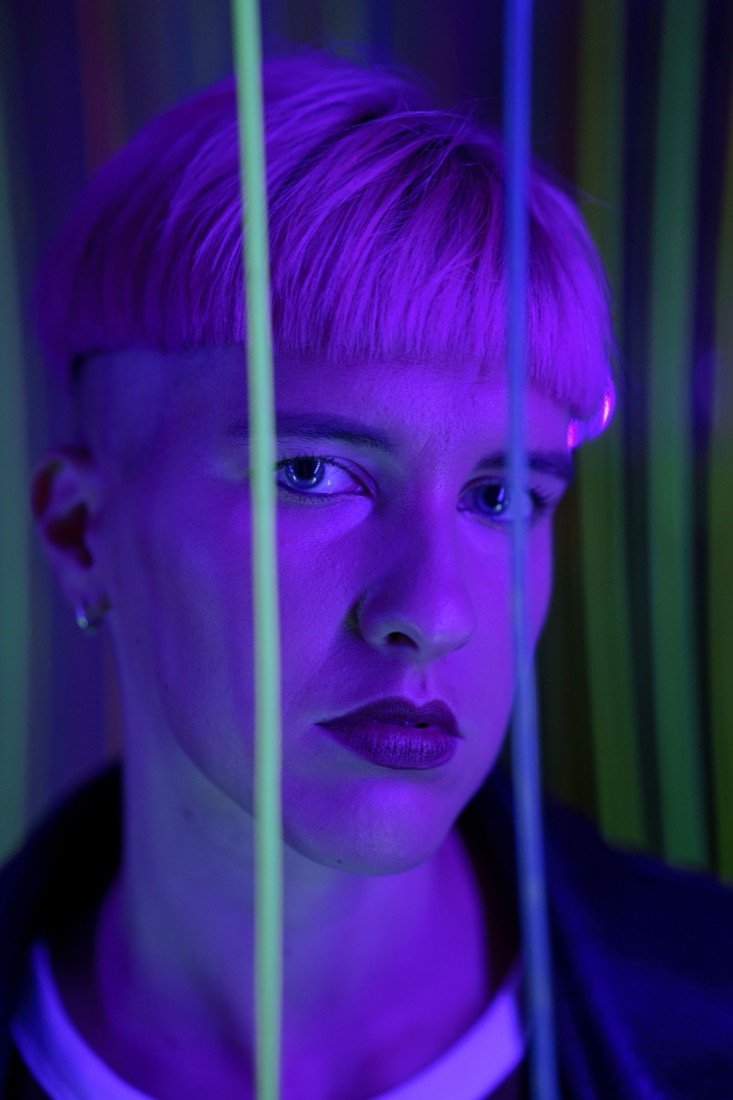 A person in violet light behind neon strands