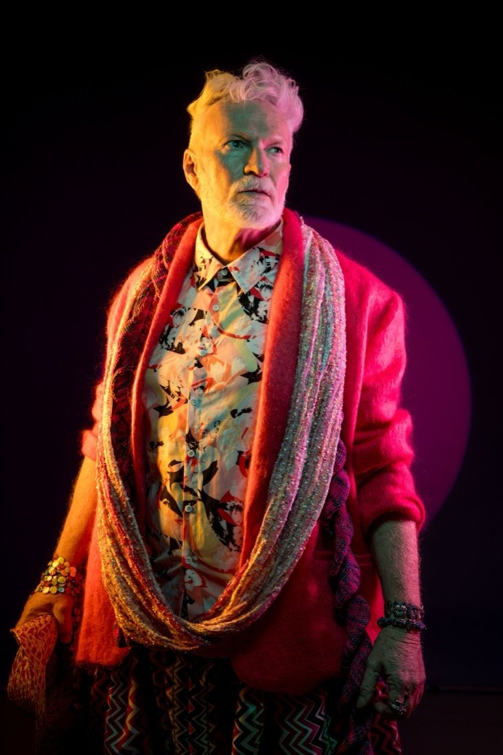 A white-haired man in pink and magenta light