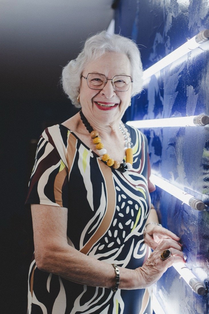 A woman with white hair, laughing, beside blue neon